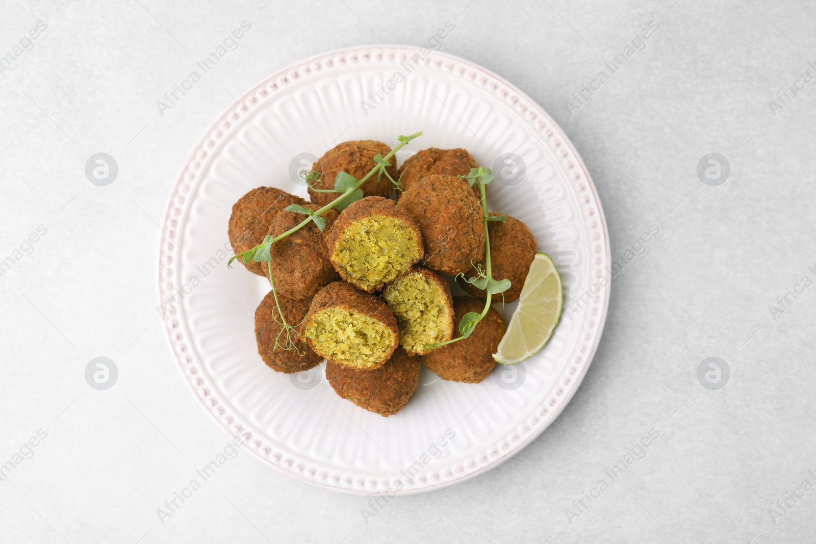 Photo of Delicious falafel balls, lime slice and microgreens on white table, top view