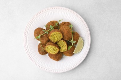 Photo of Delicious falafel balls, lime slice and microgreens on white table, top view