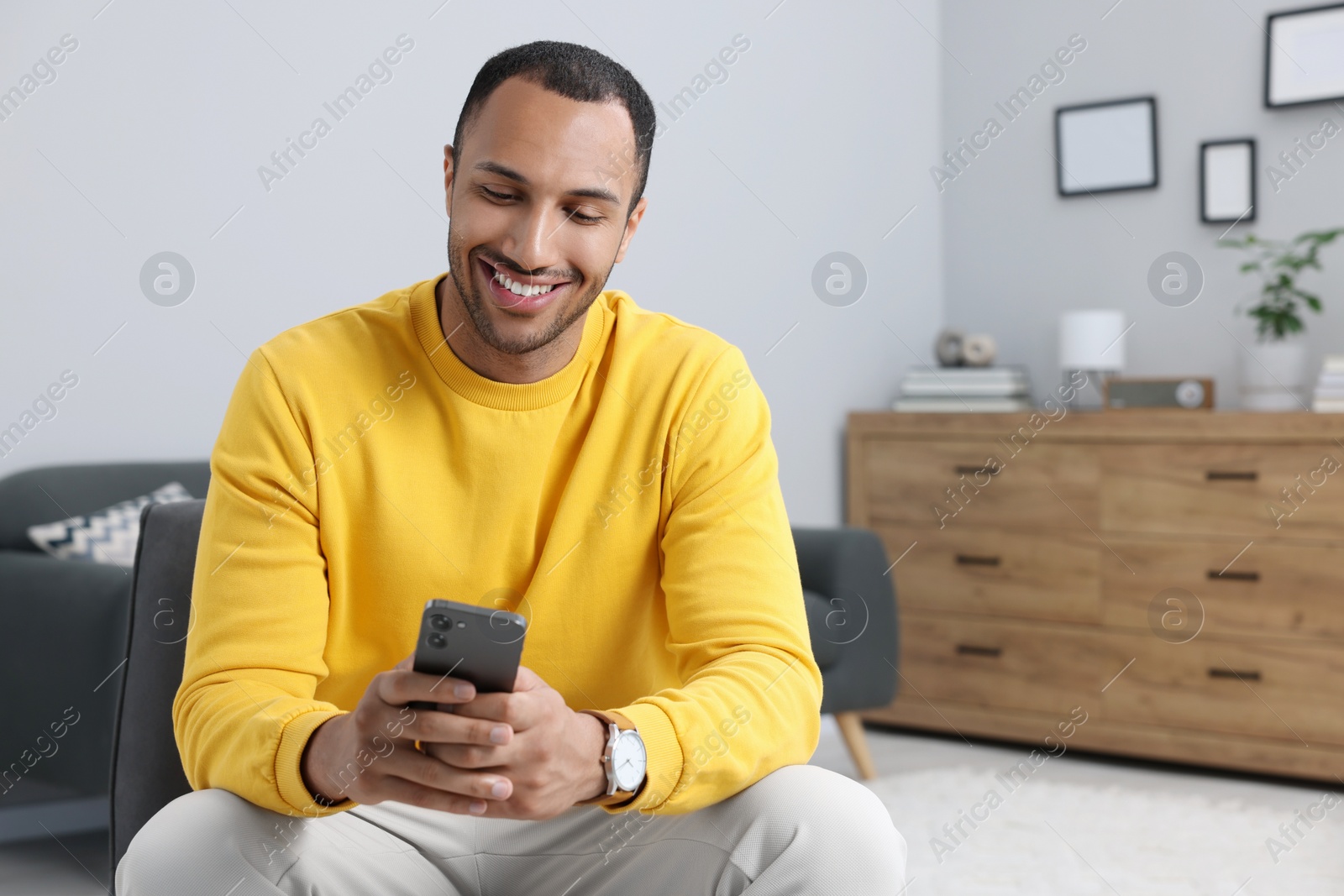 Photo of Happy man sending message via smartphone indoors