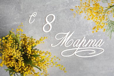 Image of Greeting card design. Beautiful mimosa flowers on grey table and text 8 March written in Russian, top view