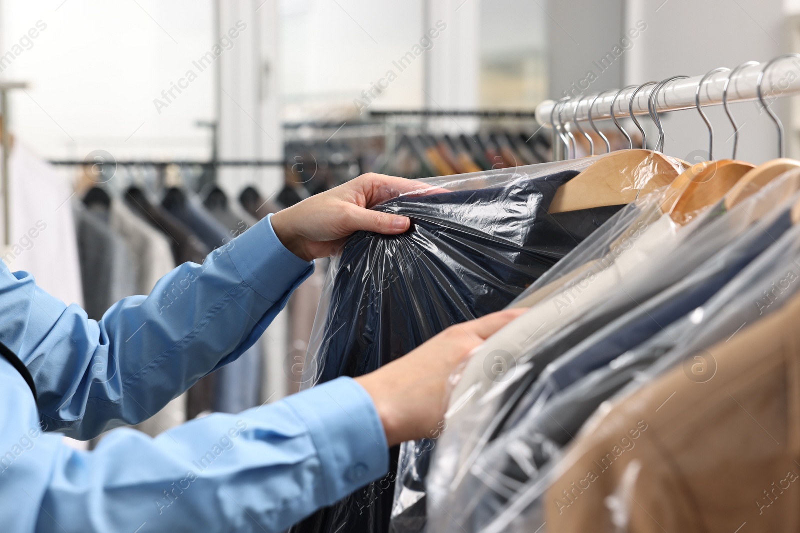 Photo of Dry-cleaning service. Woman taking jacket in plastic bag from rack indoors, closeup