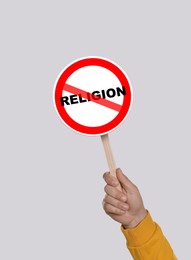 Atheism concept. Man holding prohibition sign with crossed out word Religion on light grey background