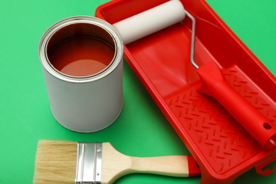 Can of orange paint, brush, roller and container on green background