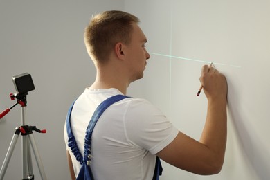 Worker using cross line laser level and pencil for accurate measurement on light wall