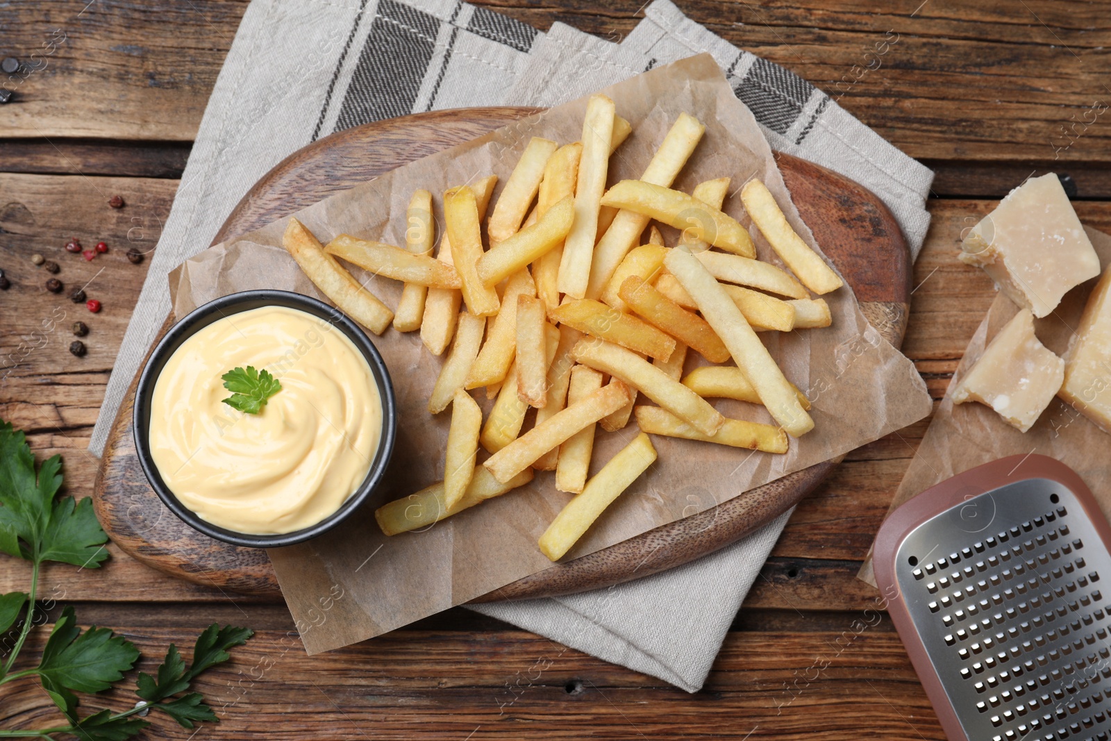 Photo of Delicious French fries and cheese sauce with parsley on wooden table, flat lay