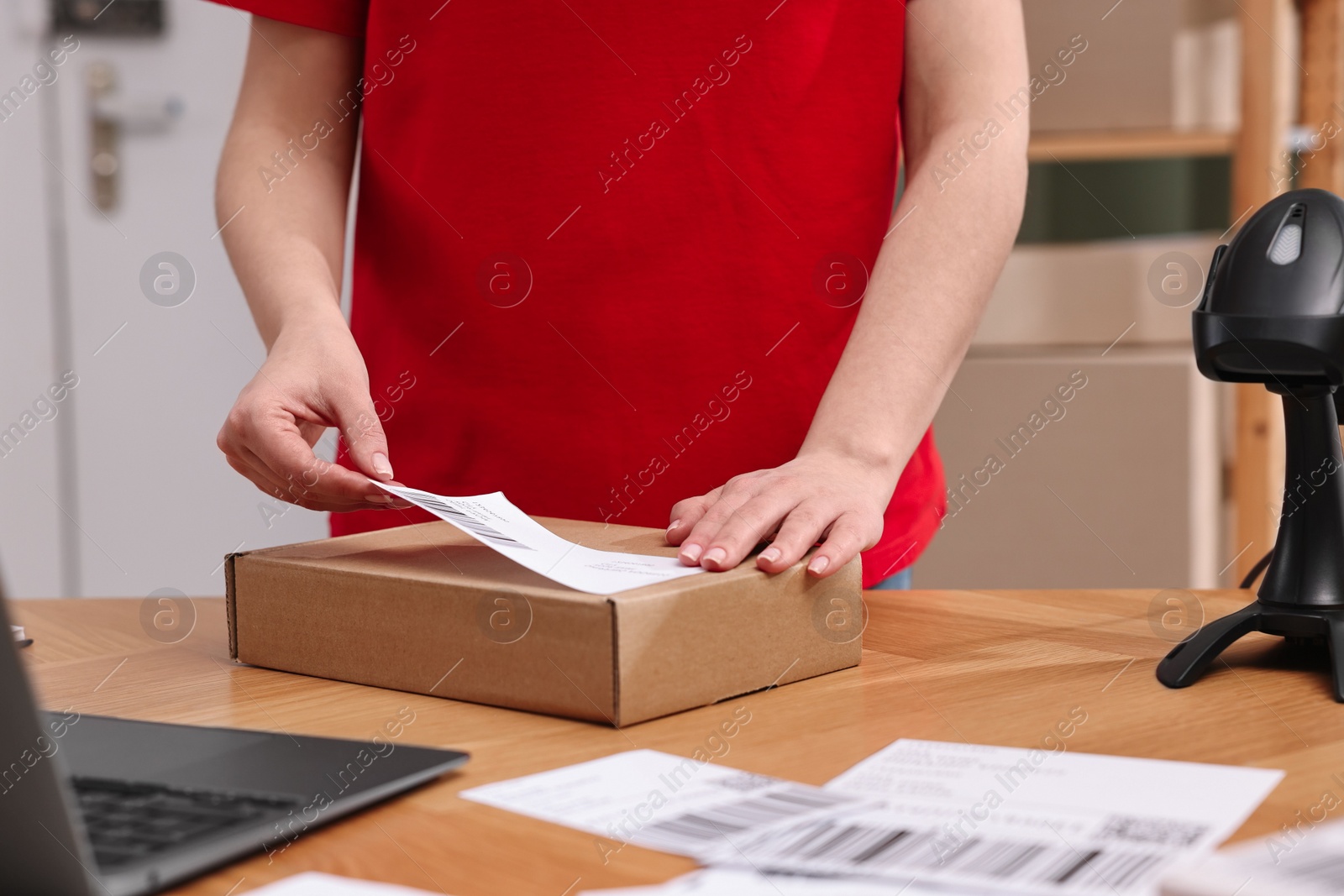 Photo of Parcel packing. Post office worker sticking barcode on box at wooden table indoors, closeup