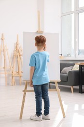 Photo of Little boy painting in studio, back view. Using easel to hold canvas