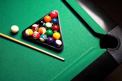 Plastic triangle rack with billiard balls and cue on green table, above view