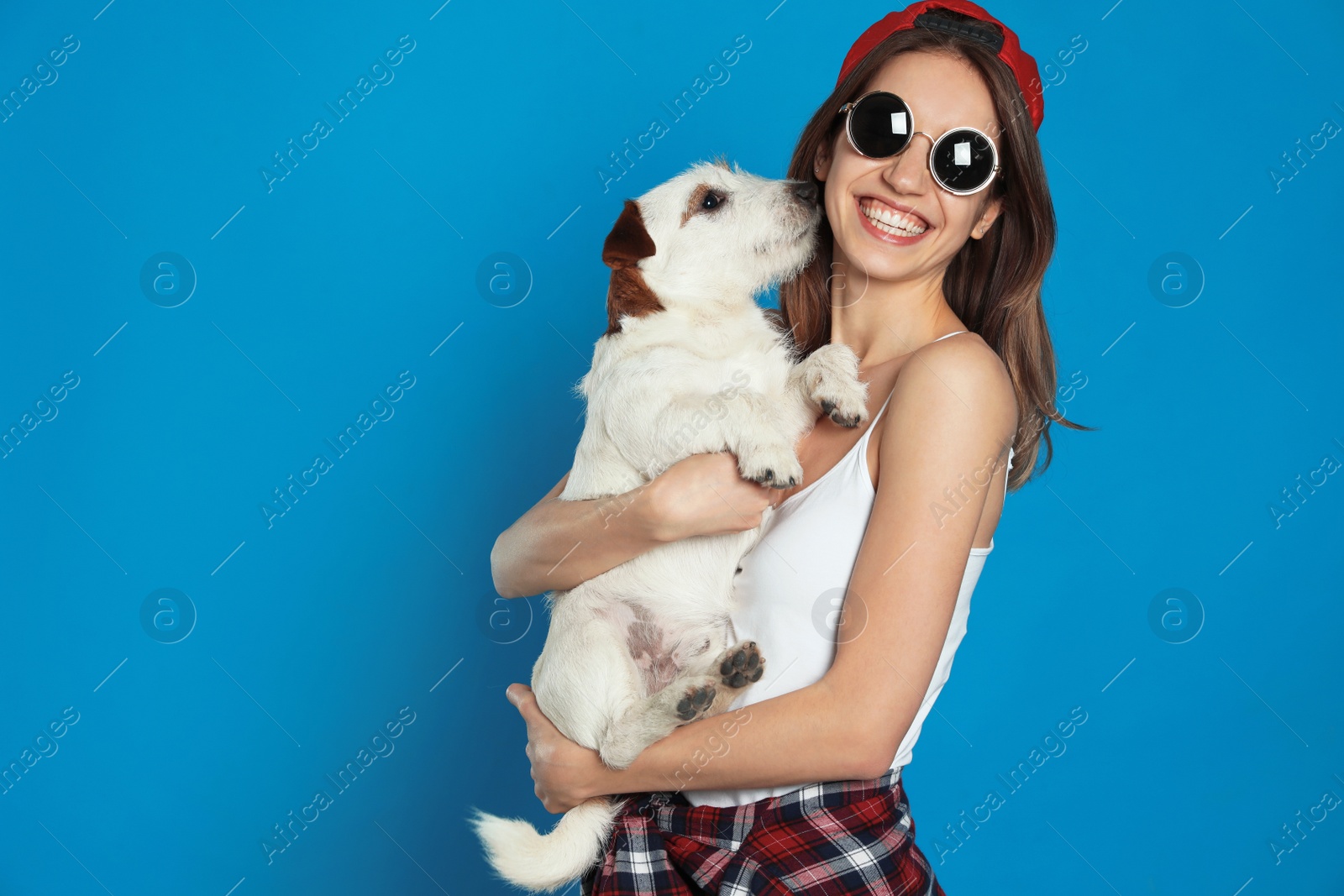 Photo of Young woman with her cute Jack Russell Terrier on light blue background. Lovely pet