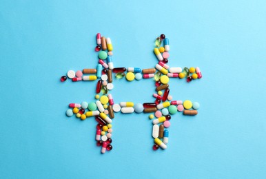 Photo of Hashtag symbol made of many different pills on light blue background, top view