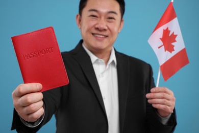 Photo of Immigration. Happy man with passport and flag of Canada on light blue background, selective focus