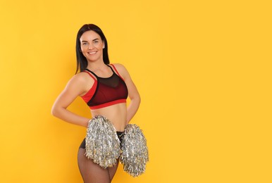 Photo of Beautiful cheerleader in costume holding pom poms on yellow background. Space for text