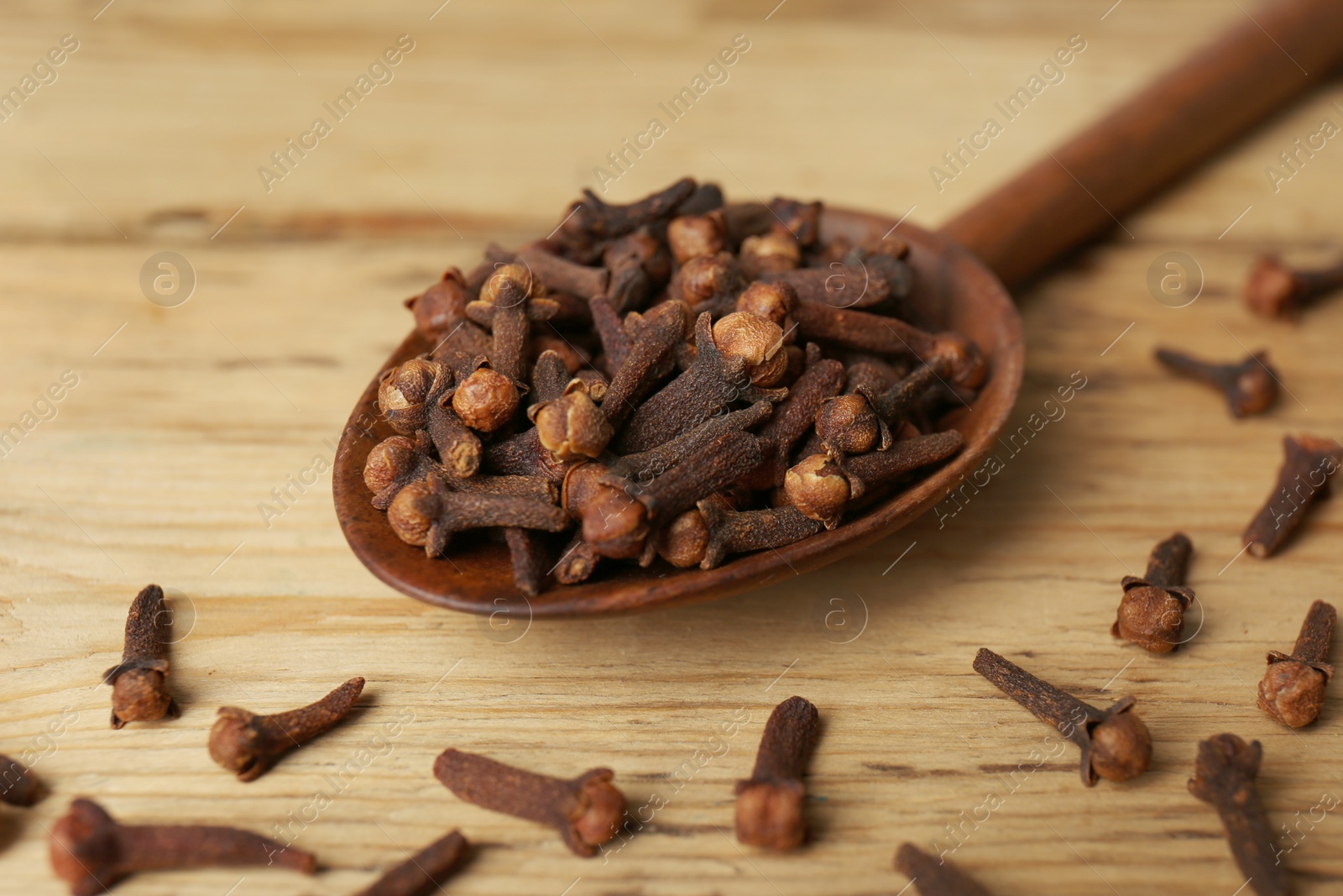 Photo of Aromatic dry cloves and spoon on wooden table, closeup