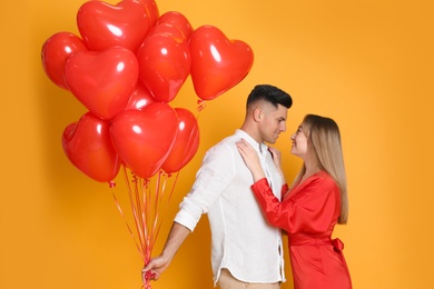 Lovely couple with heart shaped balloons on yellow  background. Valentine's day celebration