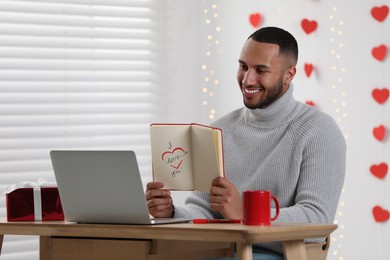 Photo of Valentine's day celebration in long distance relationship. Man having video chat with his girlfriend via laptop indoors