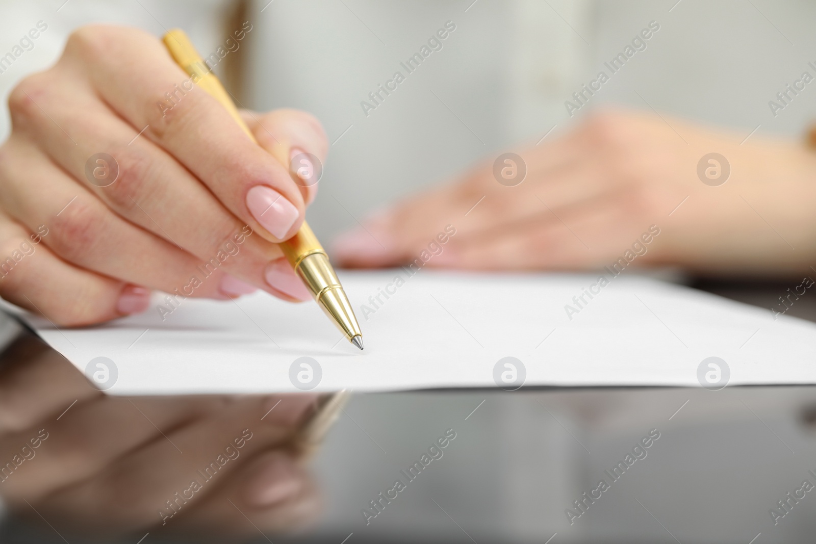 Photo of Woman writing on sheet of paper at glass table, closeup