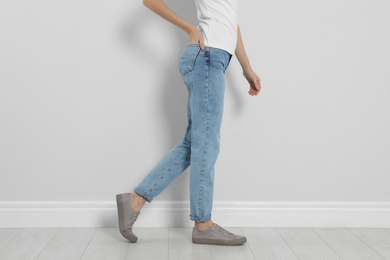Photo of Young woman in stylish jeans near light wall, closeup