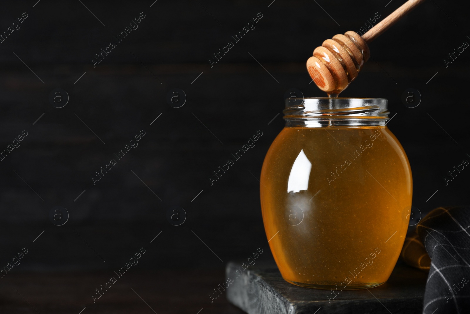 Photo of Jar of organic honey and dipper on wooden table against dark background. Space for text