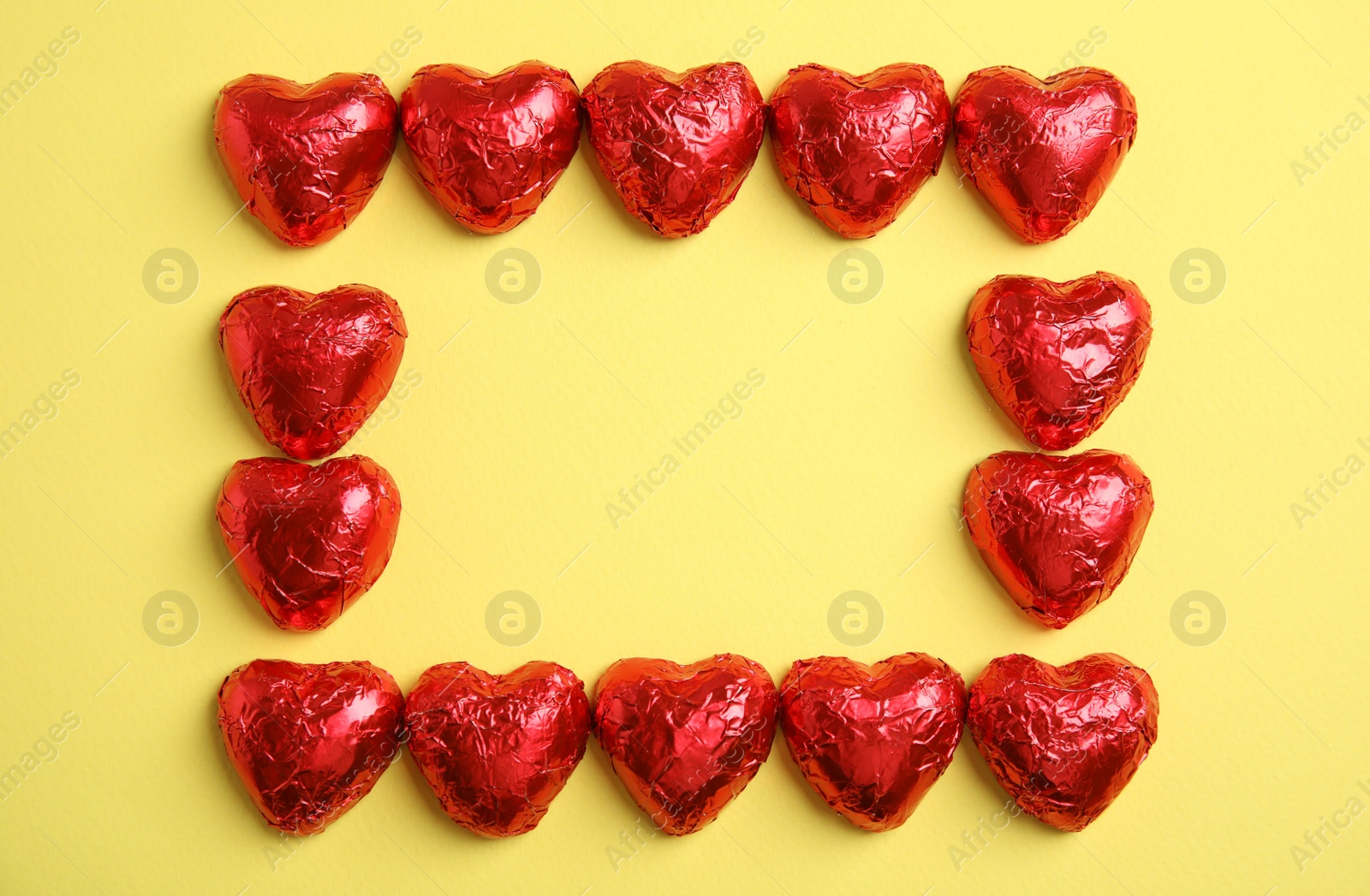 Photo of Frame of heart shaped chocolate candies on yellow background, flat lay with space for text. Valentine's day treat