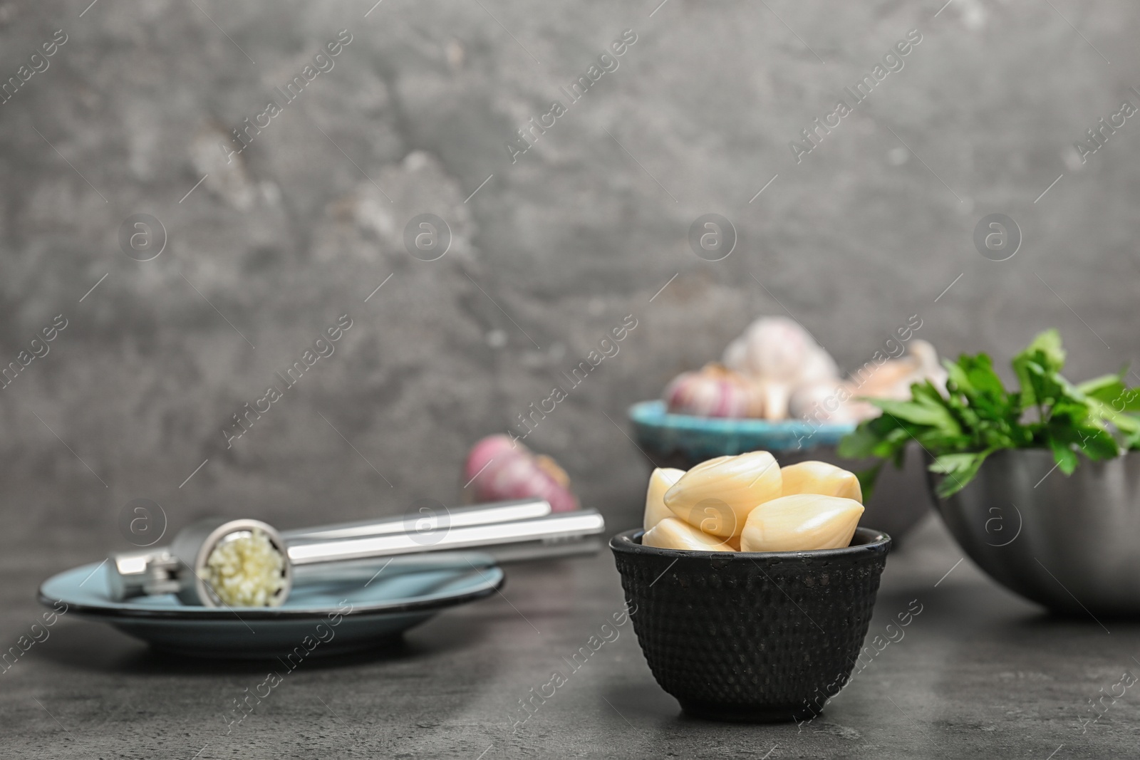 Photo of Garlic press and bowl with cloves on table