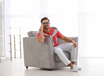 Handsome young man sitting in armchair indoors. Space for text