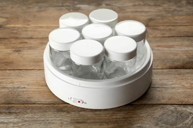 Modern yogurt maker with empty jars on wooden table