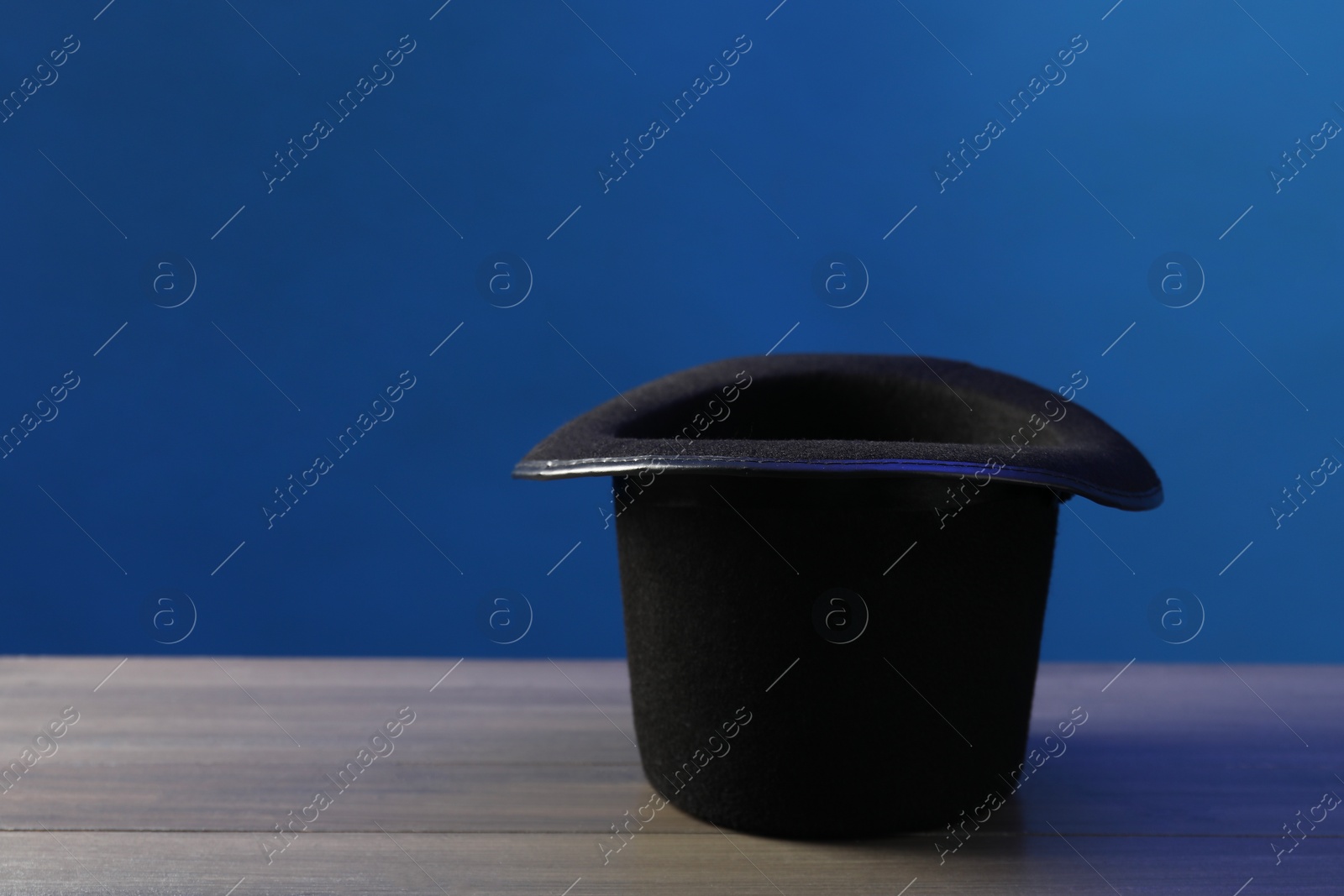 Photo of Magician's hat on wooden table against blue background, space for text