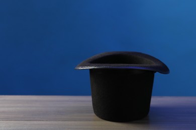 Photo of Magician's hat on wooden table against blue background, space for text