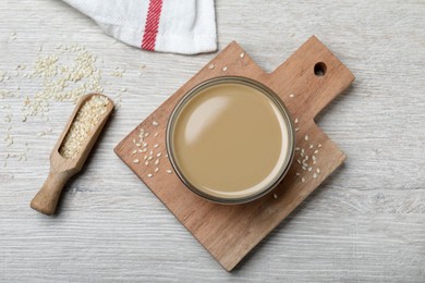 Photo of Tasty sesame paste, seeds and scoop on white wooden table, flat lay