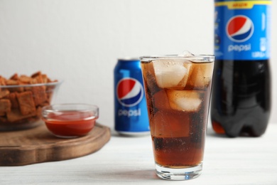 MYKOLAIV, UKRAINE - FEBRUARY 15, 2021: Glass of Pepsi and snack on white wooden table, space for text