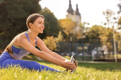 Attractive woman doing exercises on green grass in park, space for text. Stretching outdoors