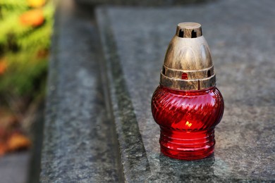 Photo of Red grave lantern with burning candle on granite surface in cemetery, space for text