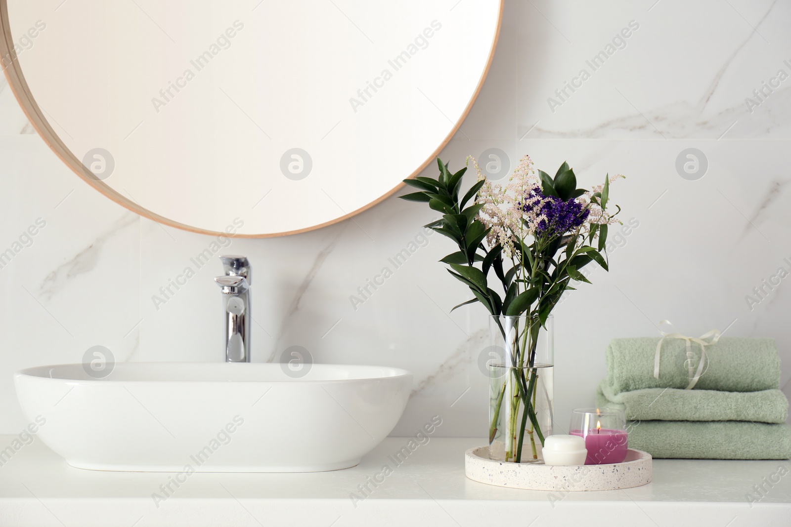 Photo of Beautiful flowers, towels and candle on countertop in bathroom. Interior decor