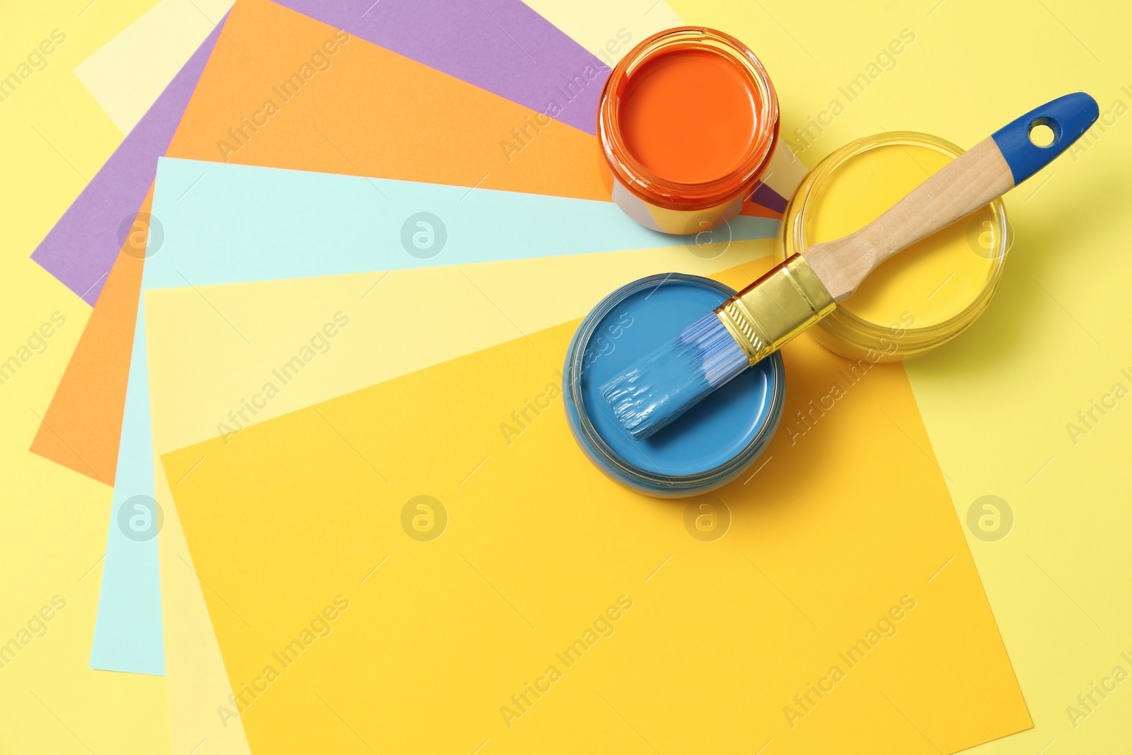 Photo of Jars of different paints and brush on color background, flat lay. Space for text