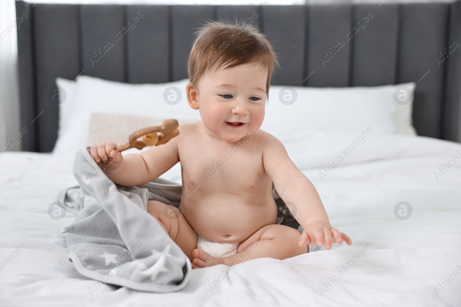 Photo of Happy baby boy with blanket and rattle sitting on bed at home