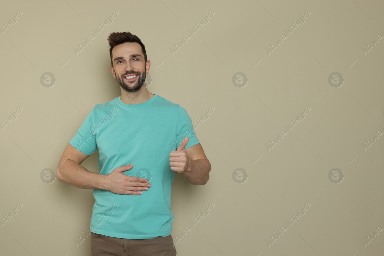 Photo of Happy man touching his belly on beige background, space for text. Concept of healthy stomach