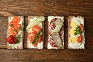 Fresh rye crispbreads with different toppings on wooden table, flat lay