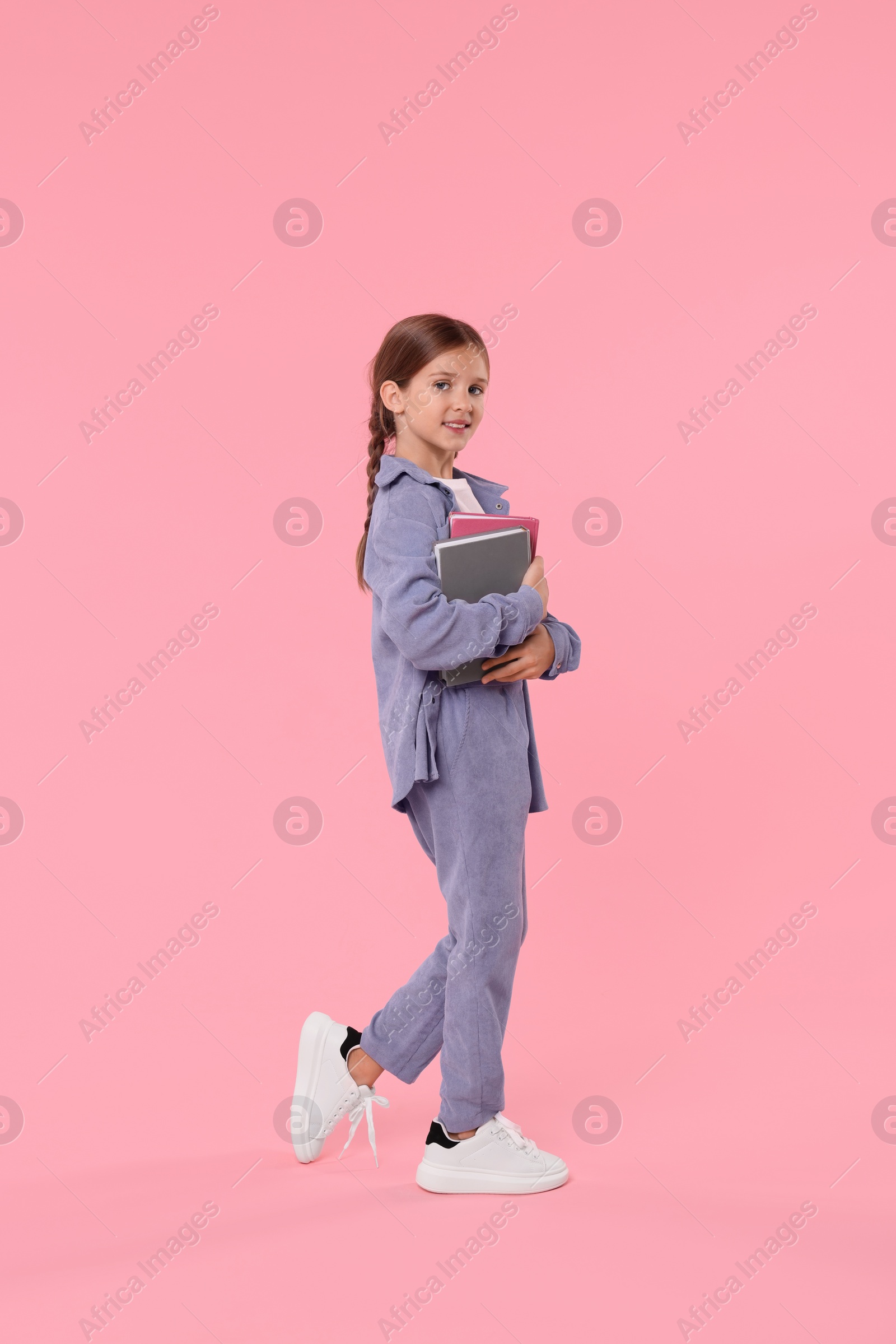 Photo of Smiling schoolgirl with books on pink background