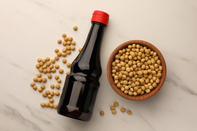 Photo of Bottle of soy sauce and soybeans on white marble table, flat lay