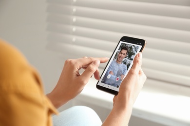Image of Woman visiting dating site via smartphone indoors, closeup