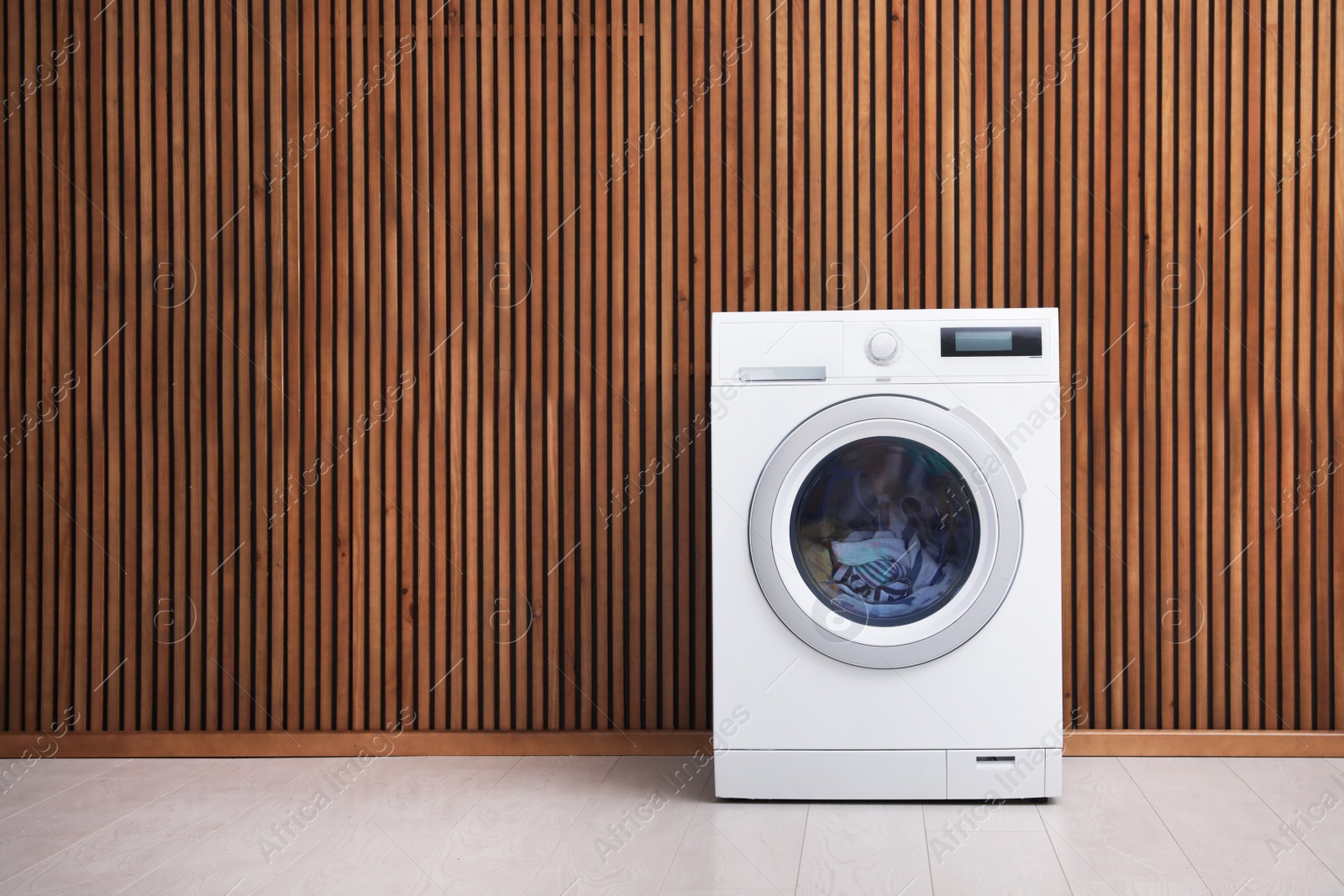 Photo of Washing machine with laundry near wooden wall. Space for text