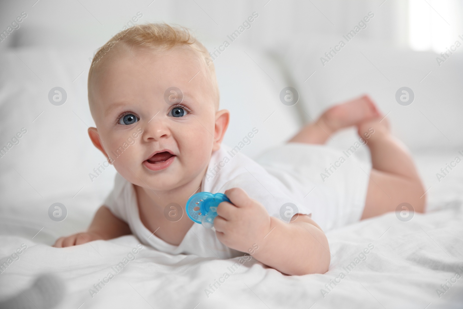 Photo of Cute baby with pacifier lying on bed at home