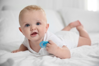 Cute baby with pacifier lying on bed at home