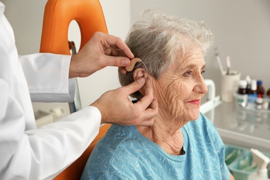 Photo of Otolaryngologist putting hearing aid in senior patient's ear at clinic