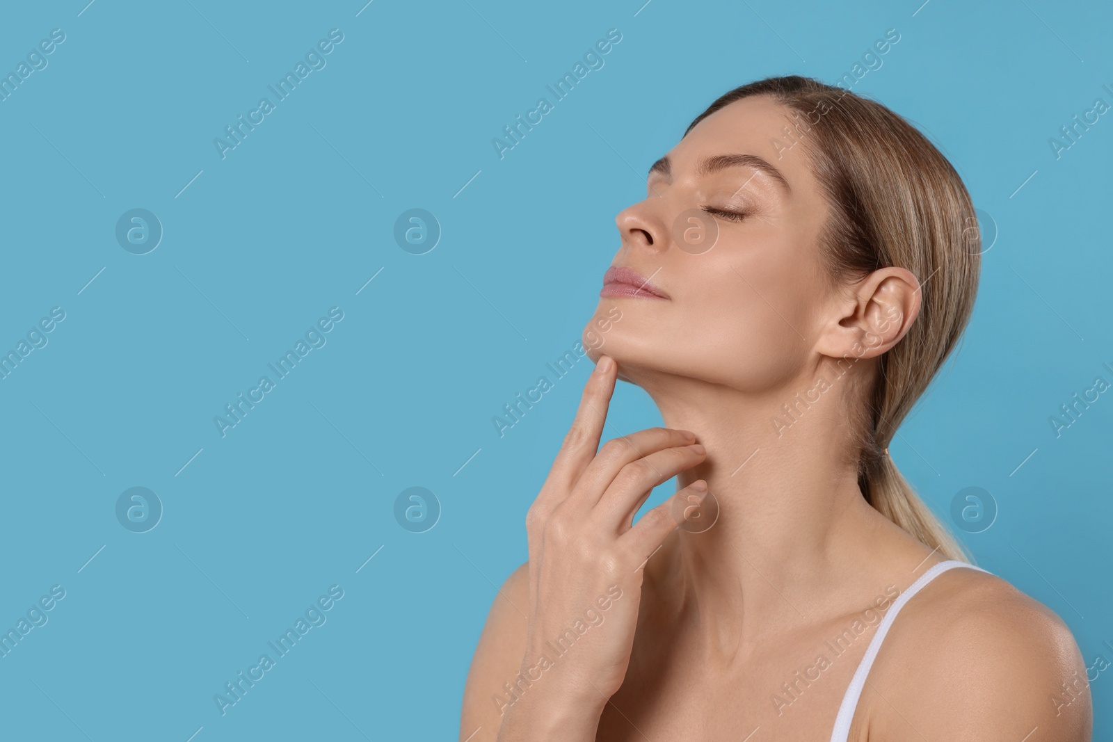 Photo of Woman massaging her face on turquoise background. Space for text