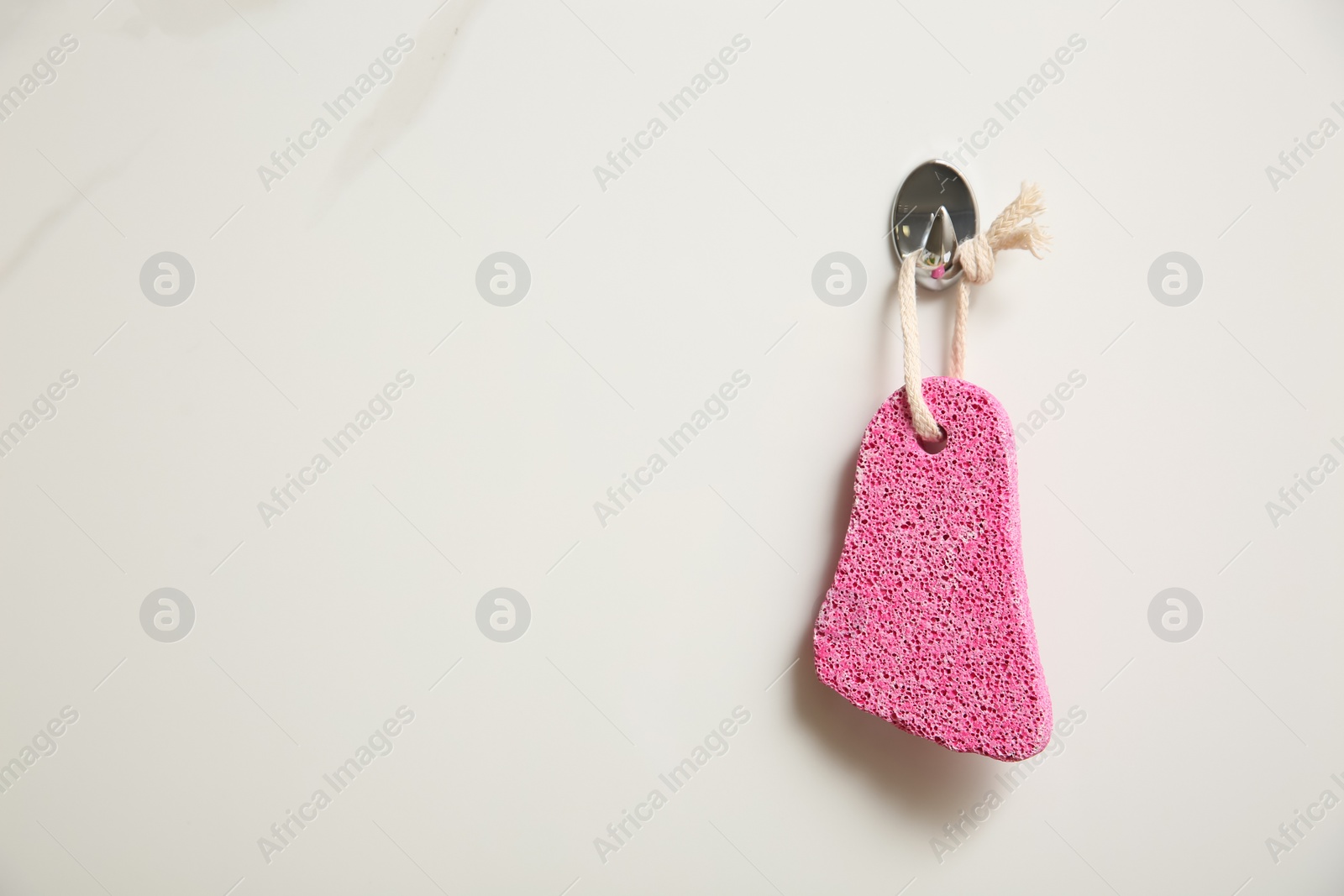 Photo of Pink pumice stone hanging on white wall, space for text