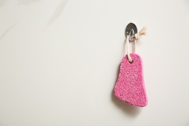 Pink pumice stone hanging on white wall, space for text