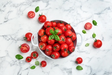 Fresh cherry tomatoes with basil leaves on white marble table, flat lay