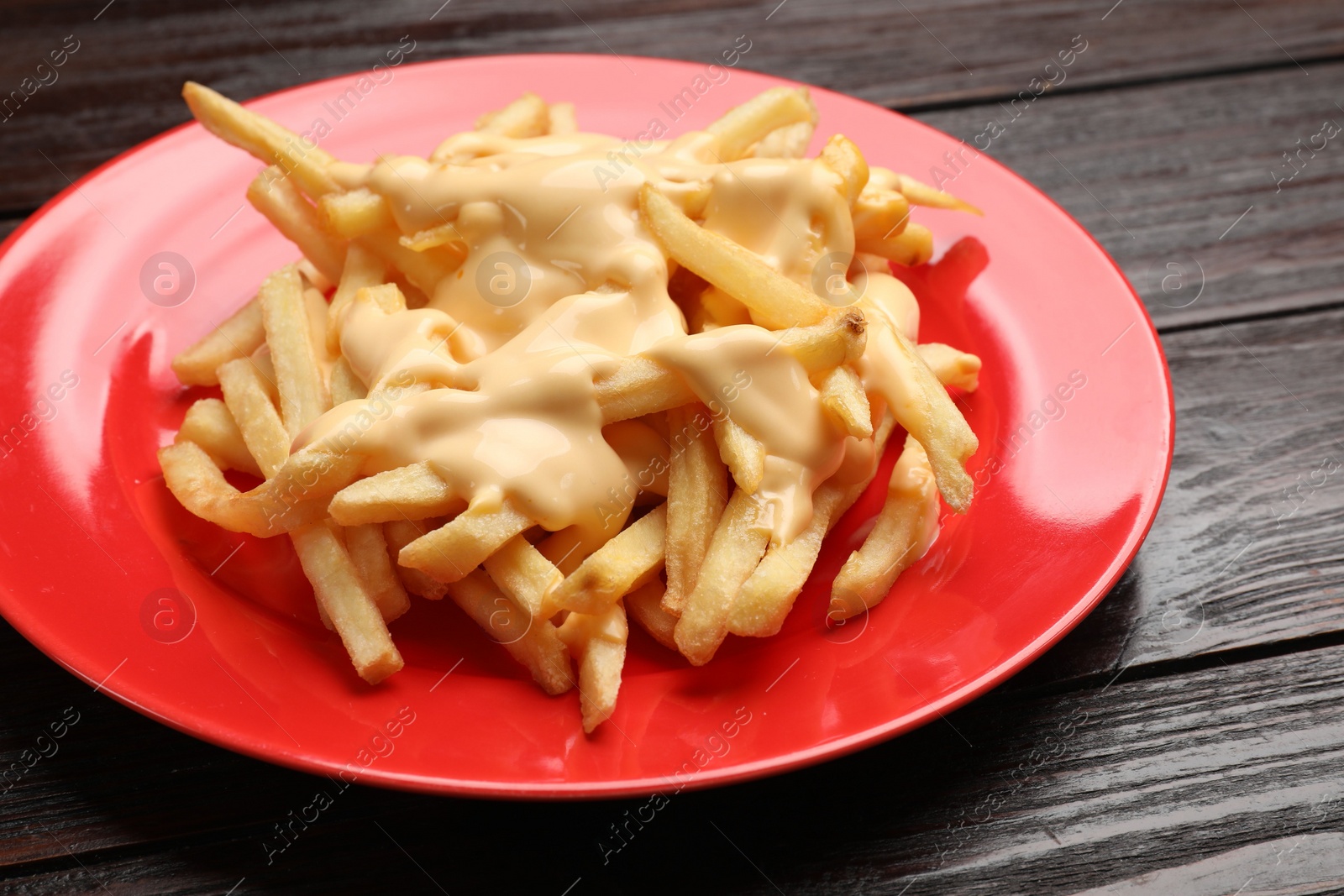 Photo of Delicious french fries with cheese sauce on wooden table, closeup