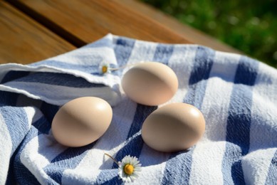 Photo of Raw duck eggs and chamomile flower with napkin on wooden table outdoors, closeup